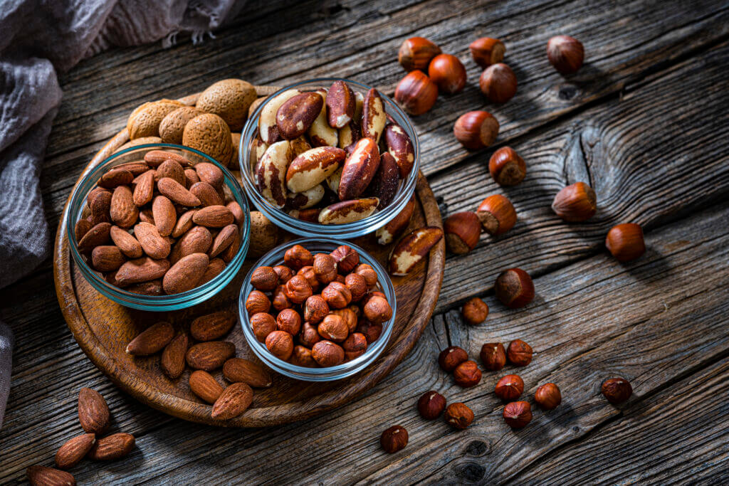 High angle view of three bowls filled with hazelnuts, almonds and Brazil nuts shot on dark rustic table. Some nuts are out the bowls spilled on the table