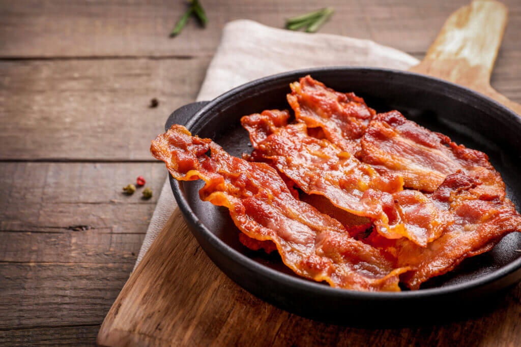bacon slices in skillet on wooden background.
