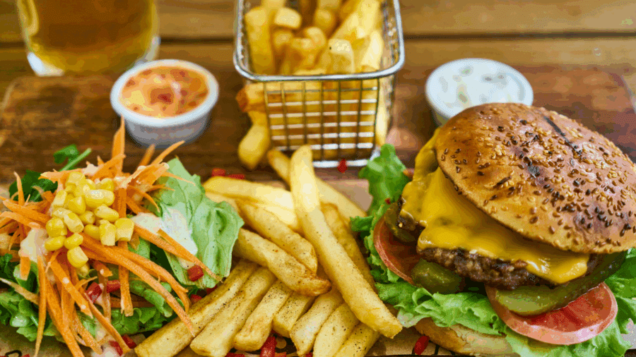 Cheeseburger and fries served on a wooden board with dipping sauce
