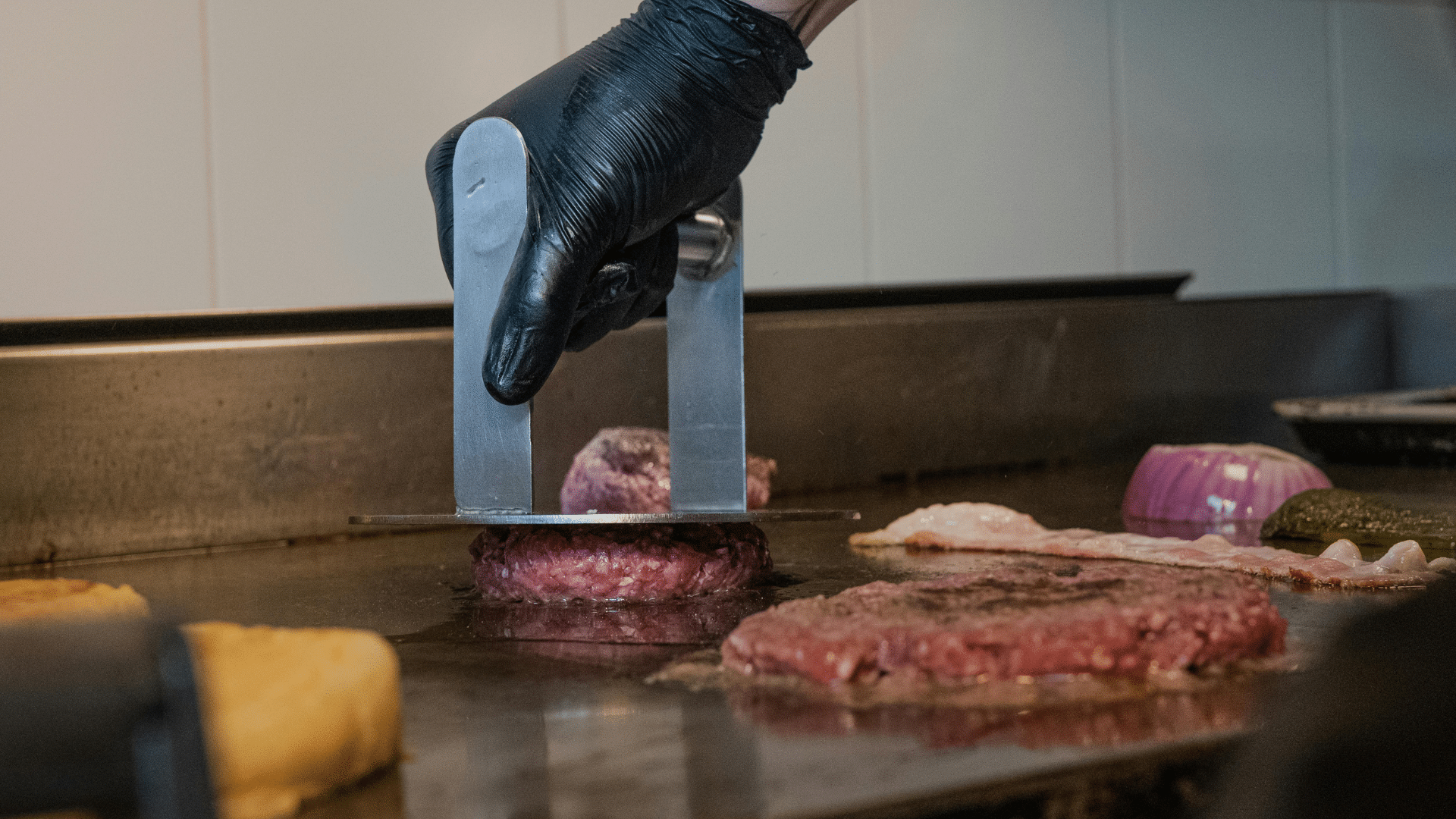 Chef preparing a gourmet burger over grill flames with tongs