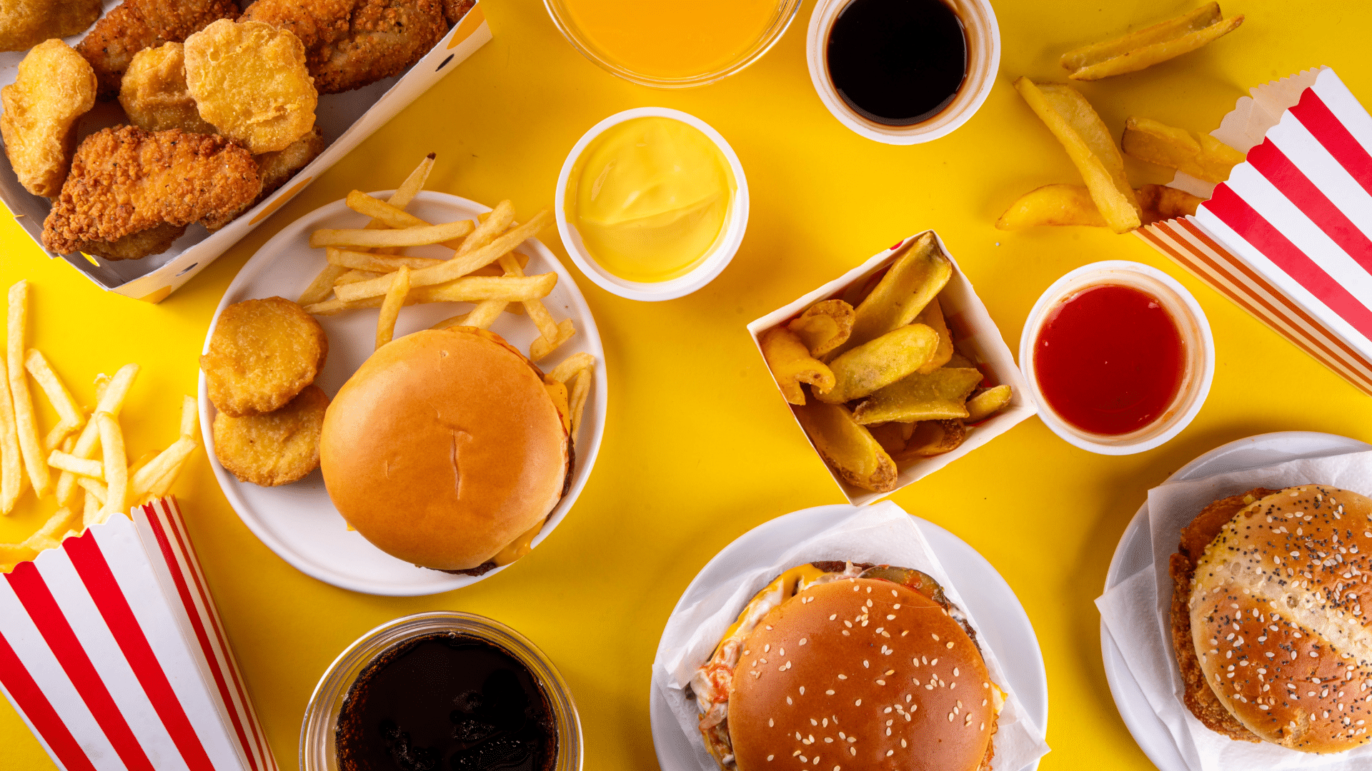 Assorted fast food items including burgers, fries, and drinks arranged on a dark surface