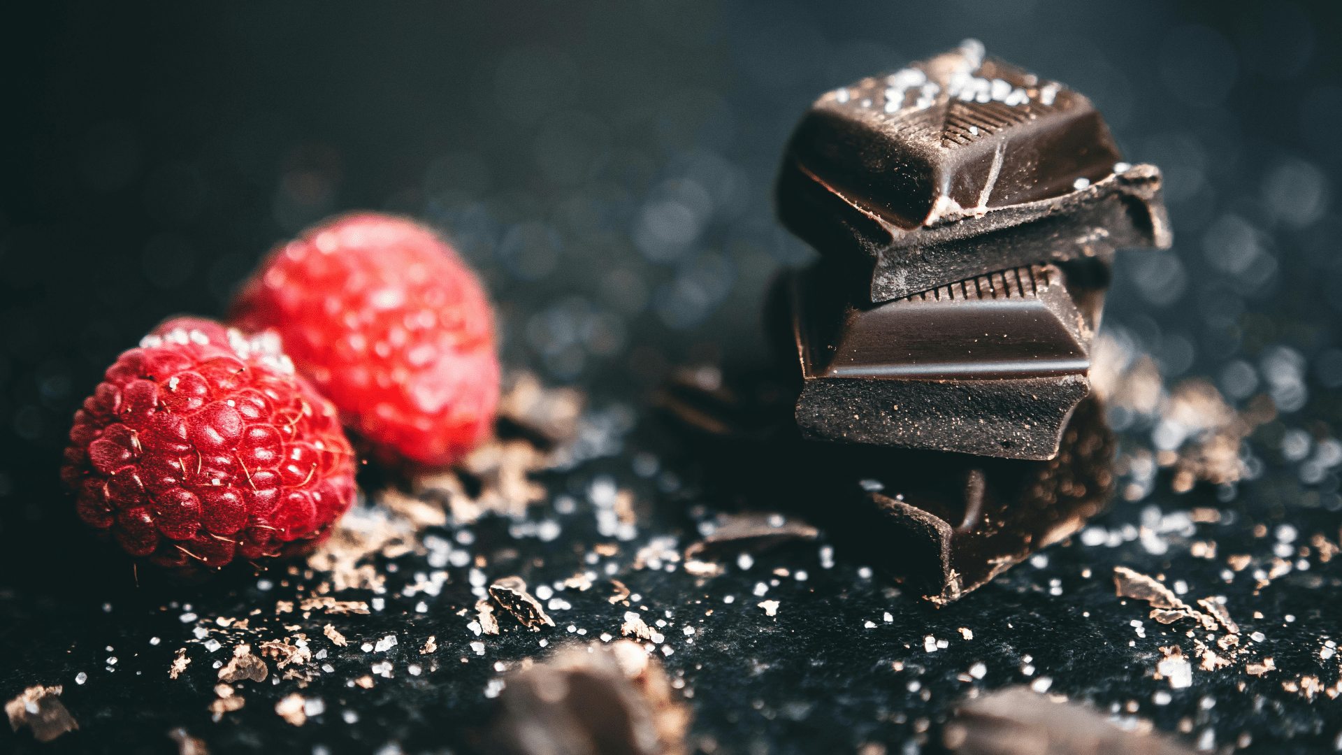 Stacked dark chocolate bars next to fresh raspberries