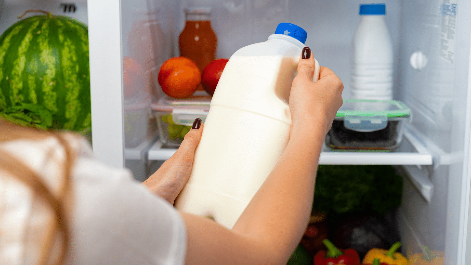 Female hand reaching for a bottle of milk inside the fridge door