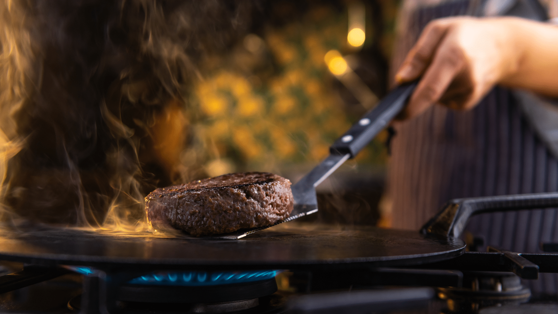 Female chef flipping burgers on a hot griddle in a professional kitchen