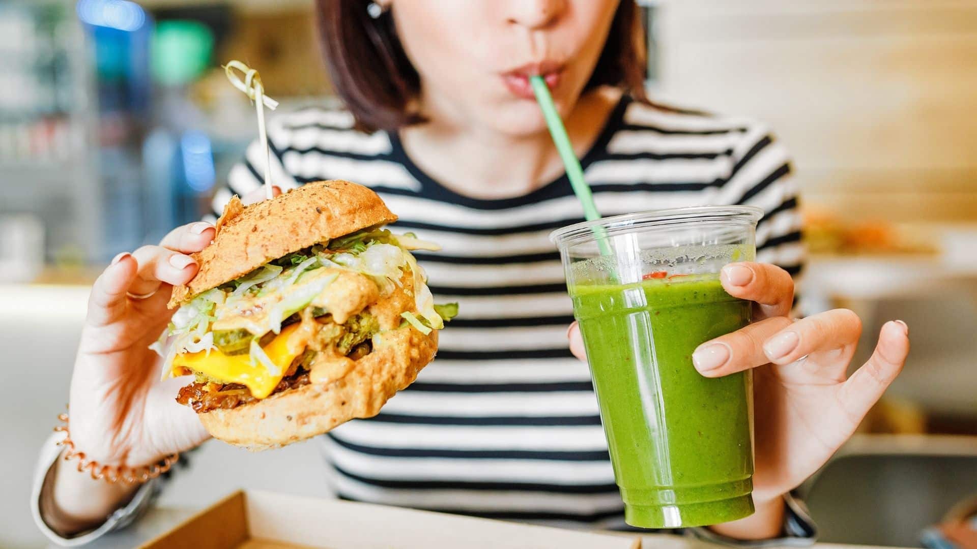 A young woman drinks green smoothies and eats a burger in a vegan fast food restaurant