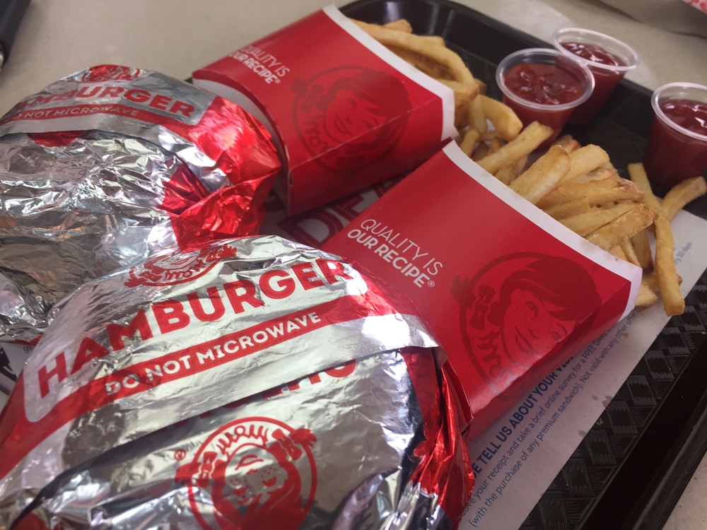 Wendy’s wrapped hamburgers and fries served with ketchup cups on tray.