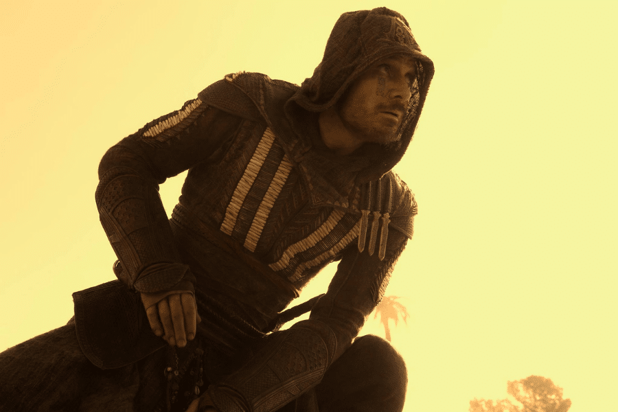 A mysterious figure in a hooded cloak crouches against a warm, golden-hued sky. The intricate armor suggests a sense of readiness and stealth.