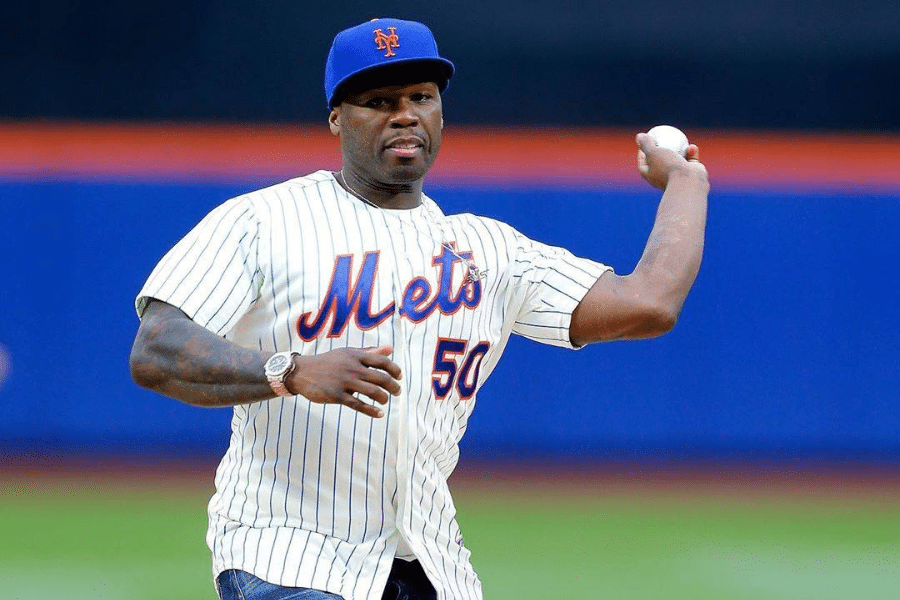 Man in a Mets jersey and cap throws a baseball on a field. He appears focused, with a crowd and a vibrant stadium background visible.