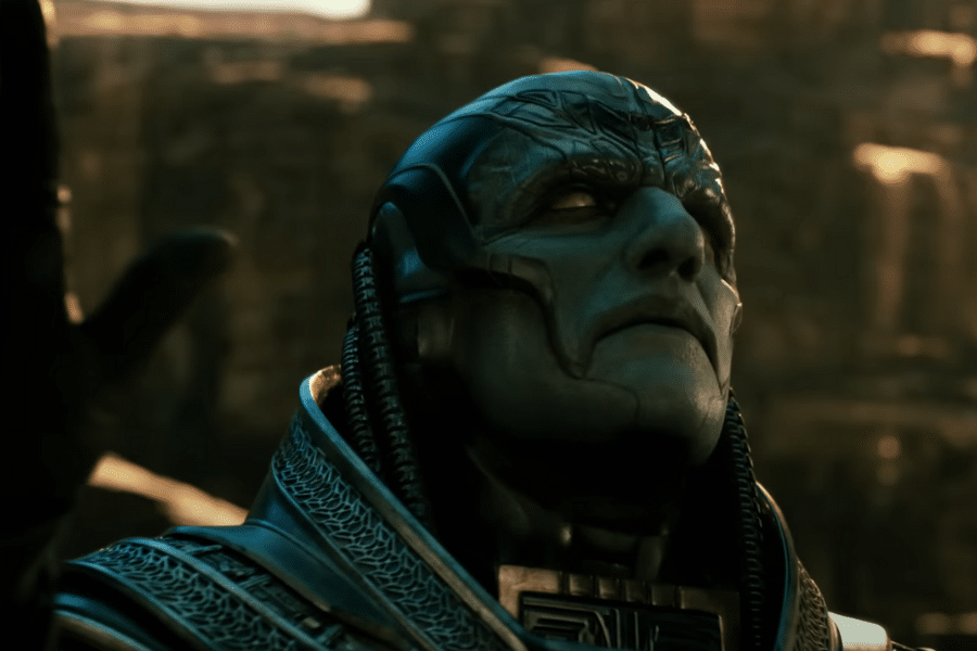 An alien-like figure with a detailed, sculpted face and headgear gazes upwards in a rocky, sunlit background, conveying a sense of power and contemplation.
