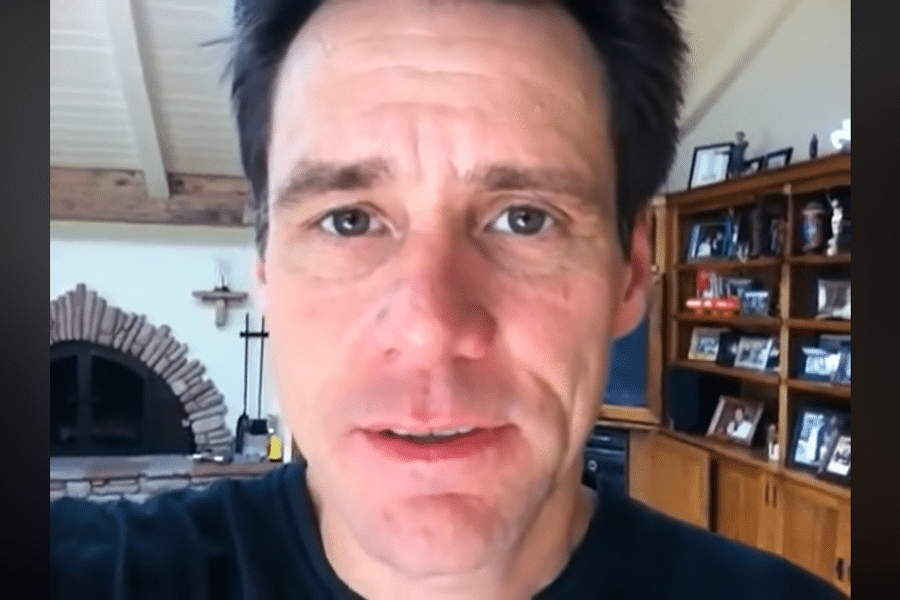 A person with short dark hair in a close-up, casual expression, inside a warmly lit room with wooden shelves and a brick fireplace in the background.