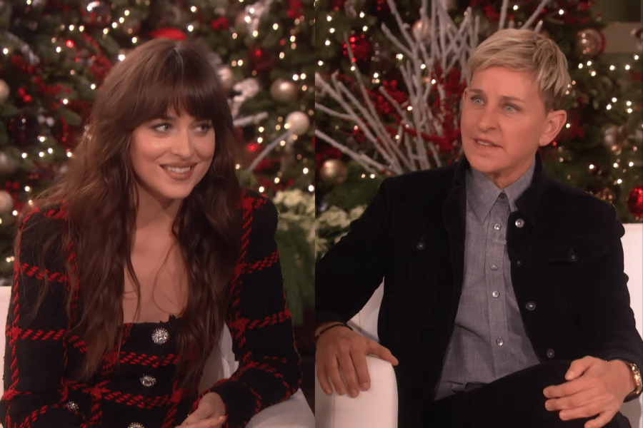 Two people sit on a talk show set decorated for the holidays. They are talking and smiling, with festive trees and lights in the background.