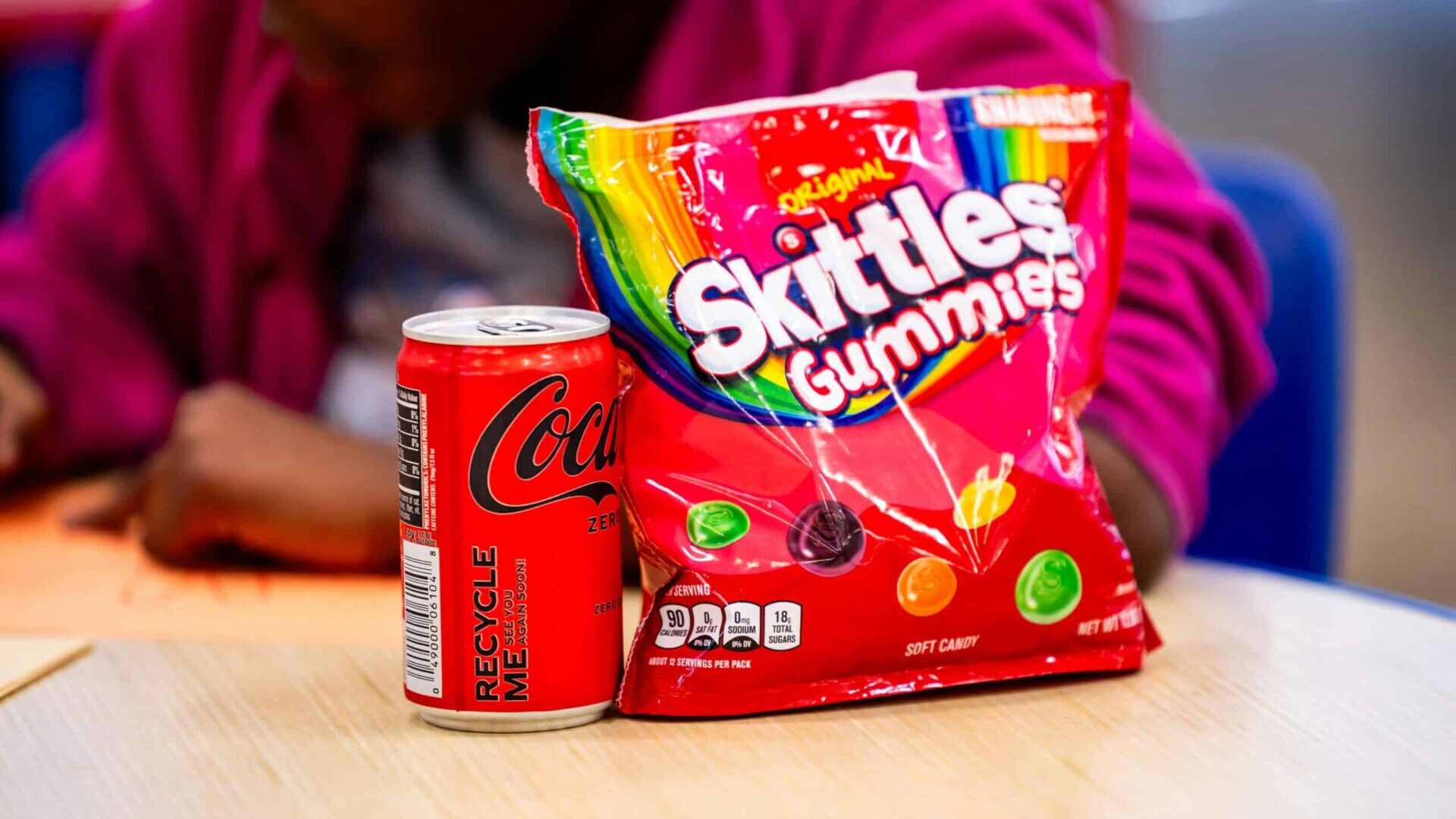 A can of Coca-Cola Zero Sugar with Skittles gummies on a table indoors