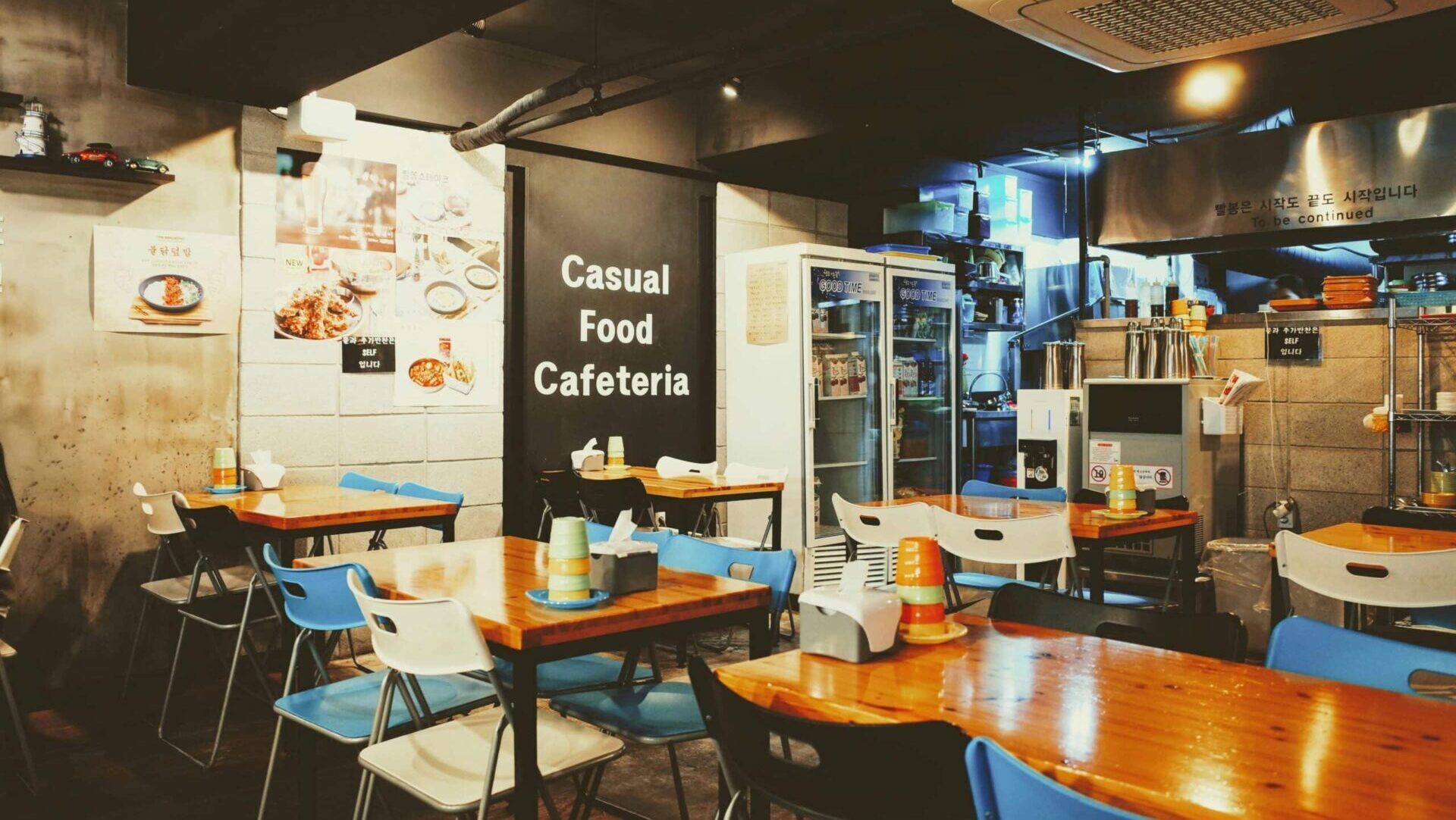 Interior view of an empty restaurant with wooden tables and chairs arranged neatly in rows inside a cozy, modern dining space.