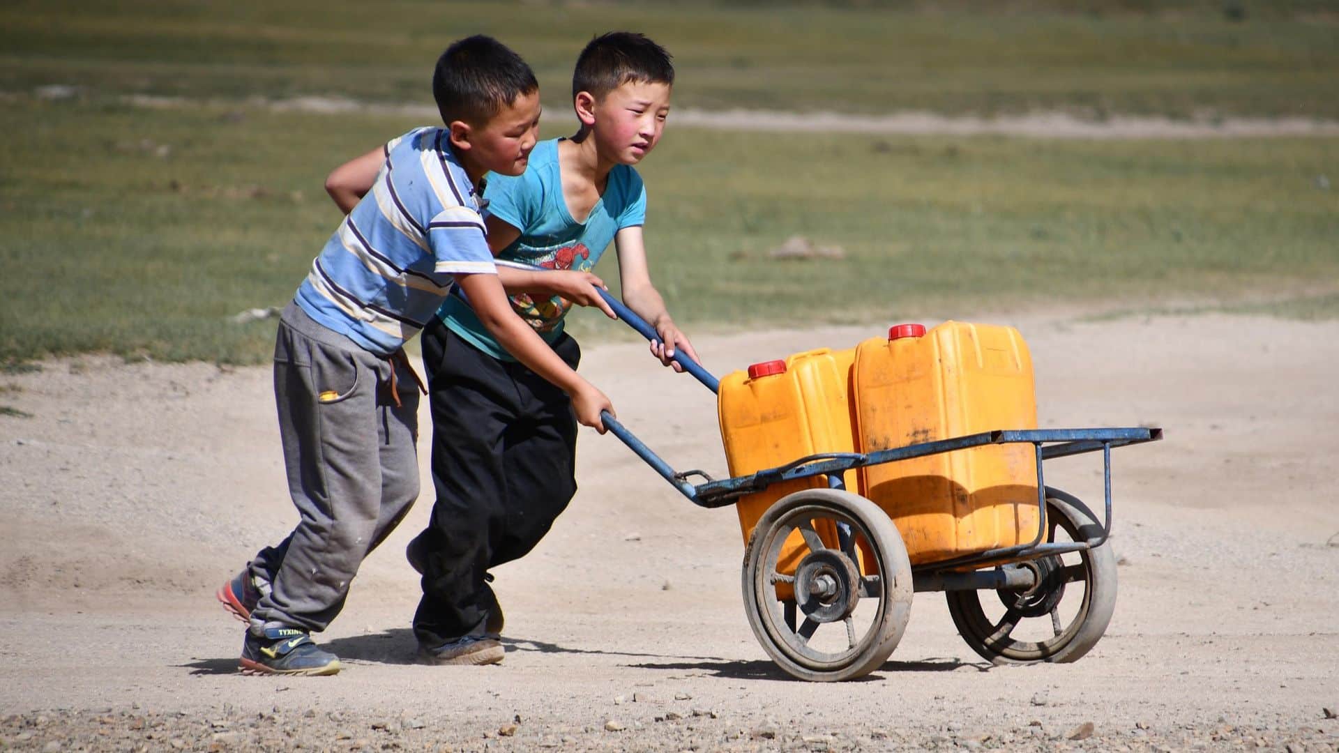 Children carrying large water containers in a rural outdoor area