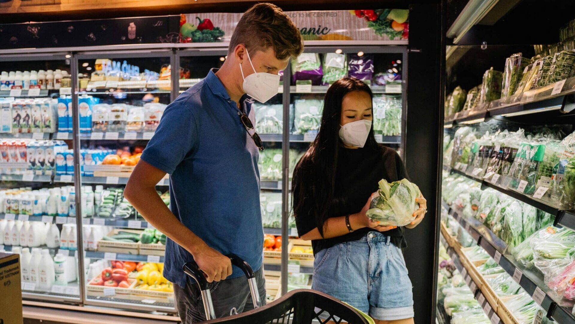 Couple shopping for vegetables inside a grocery store, choosing produce together.