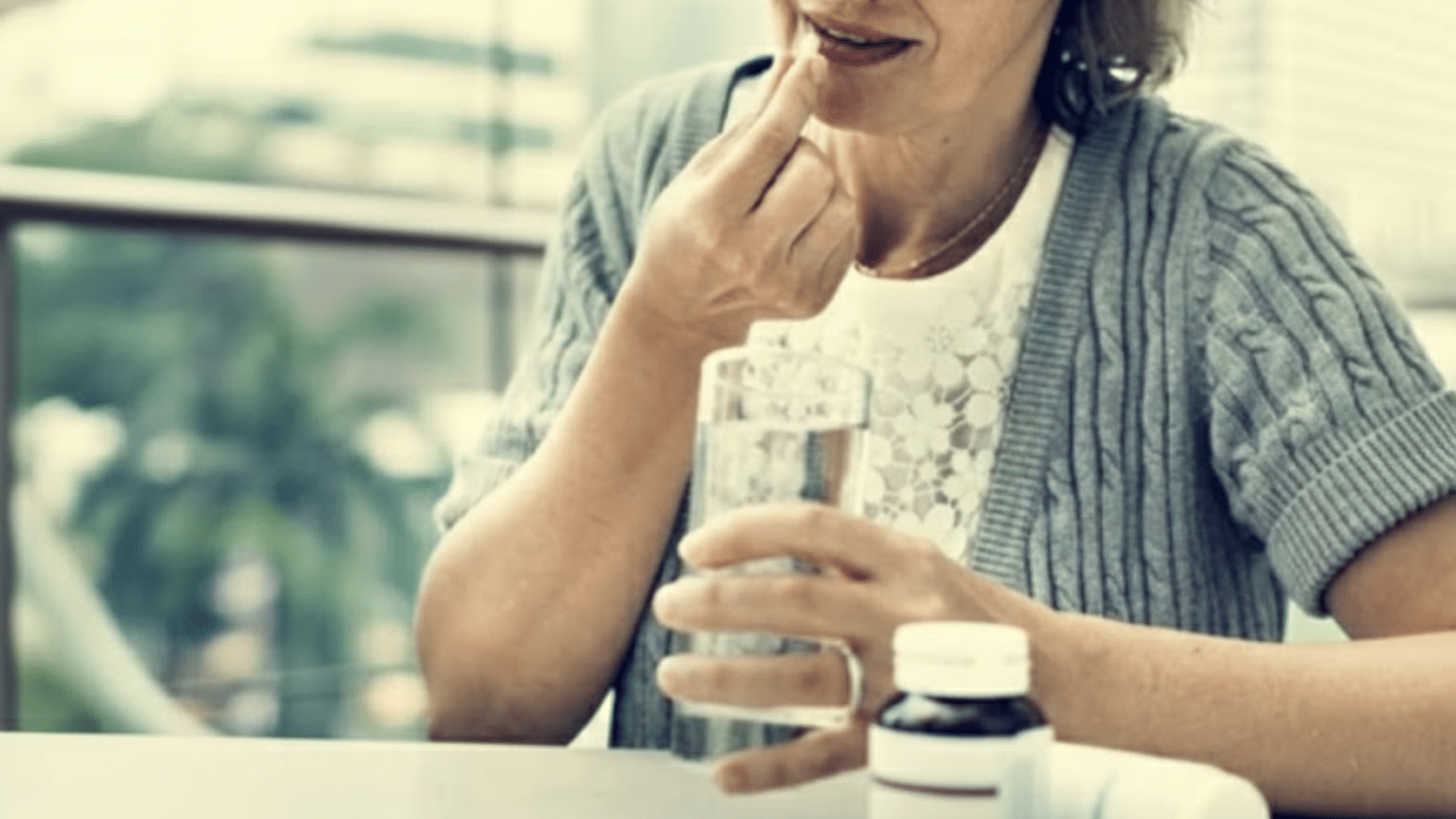 Woman holding a pill and a glass of water at a table.