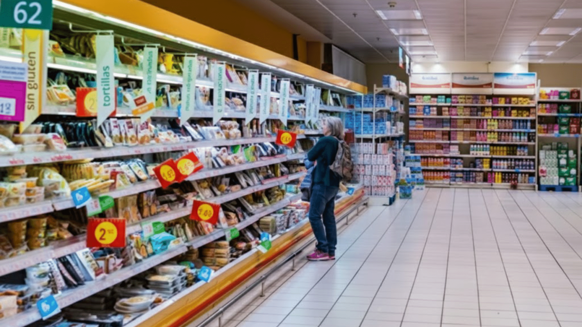 Woman standing in a supermarket aisle looking at tortilla packages.