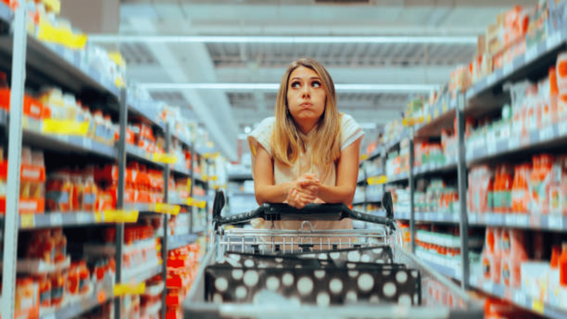 Woman leaning on a shopping cart with a stressed expression in a grocery aisle.
