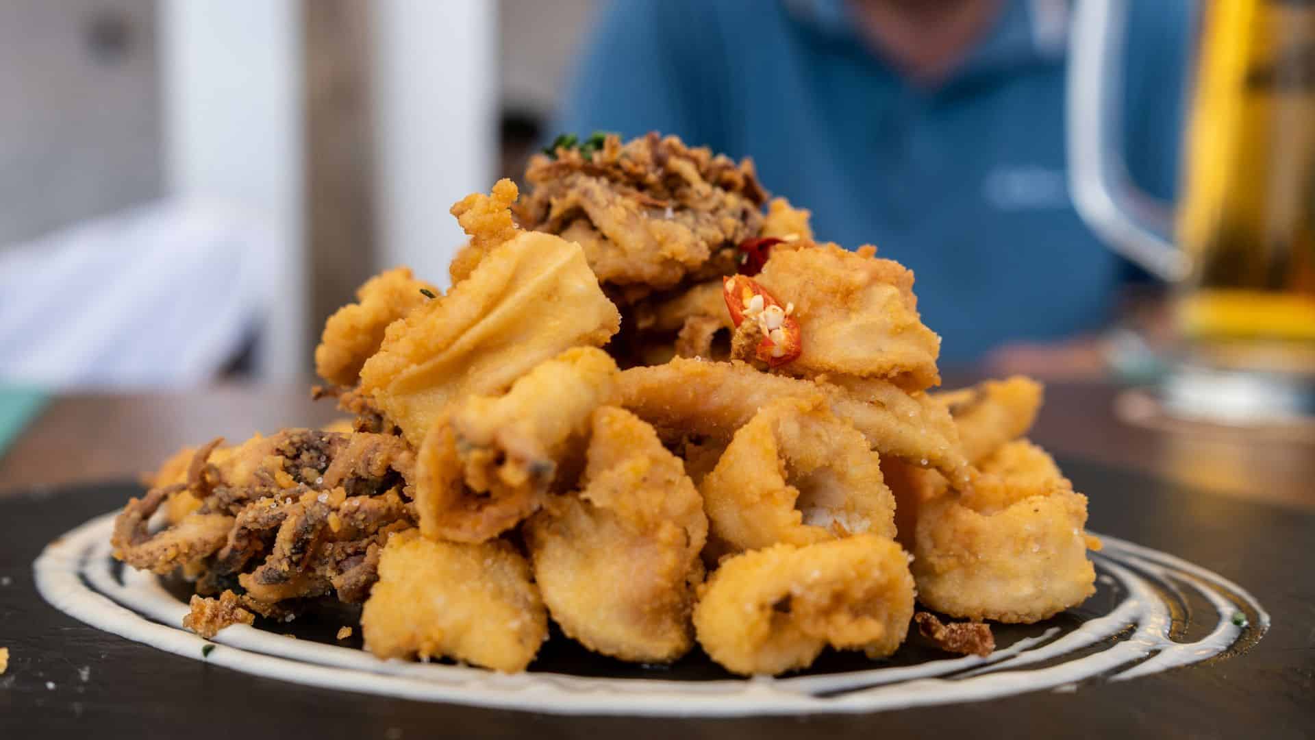 Pile of fried calamari served on a dark plate with textured coating