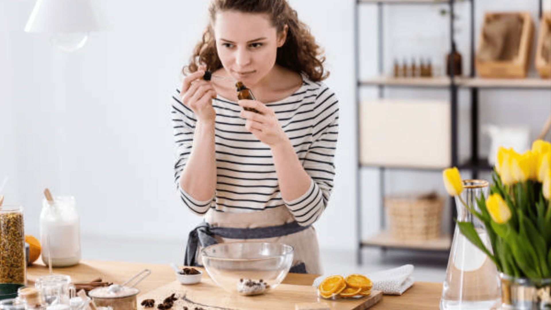 Woman smelling a dropper bottle while standing in a bright kitchen.