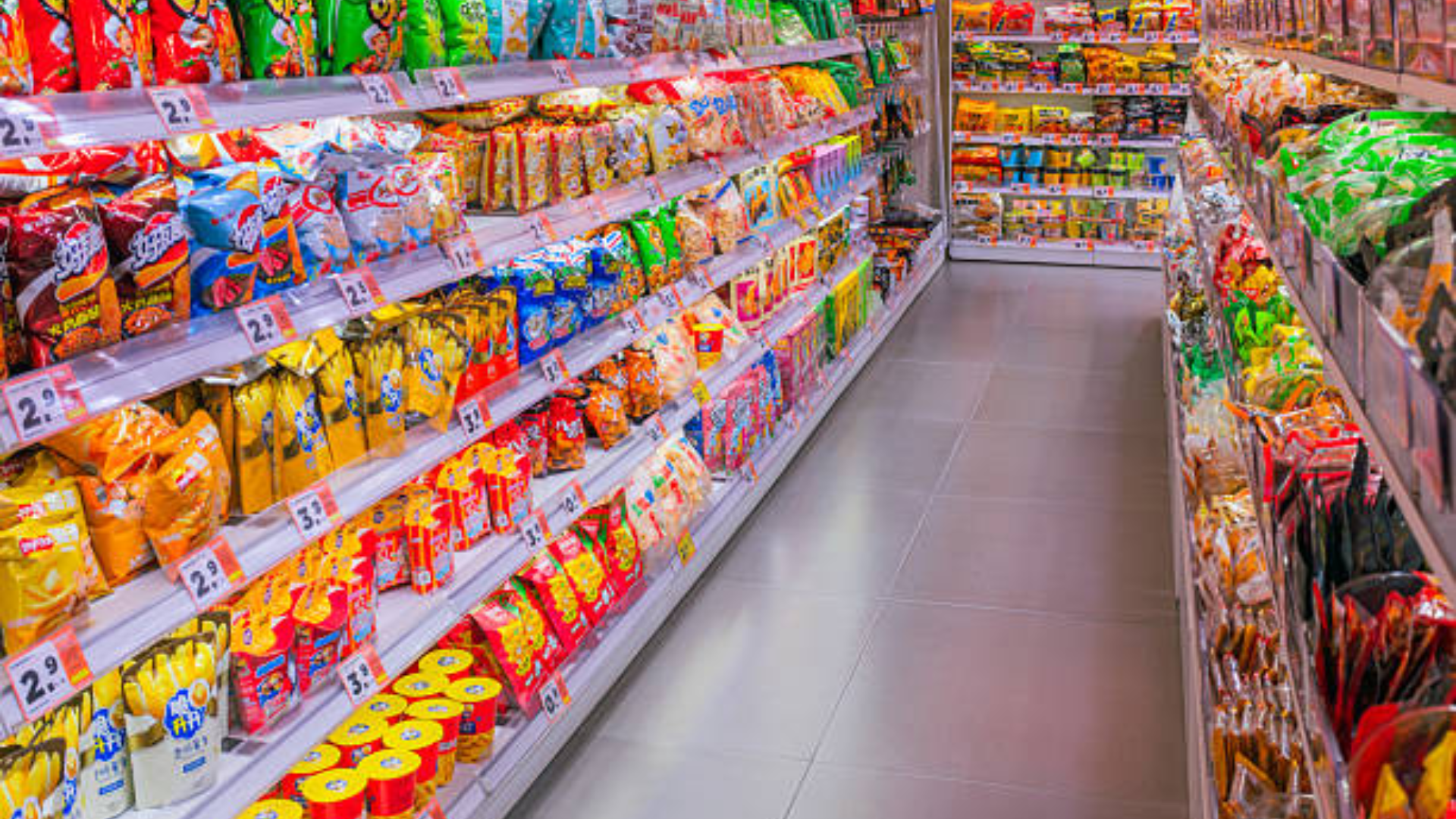 Colorful snack packages displayed on both sides of a supermarket snack aisle.
