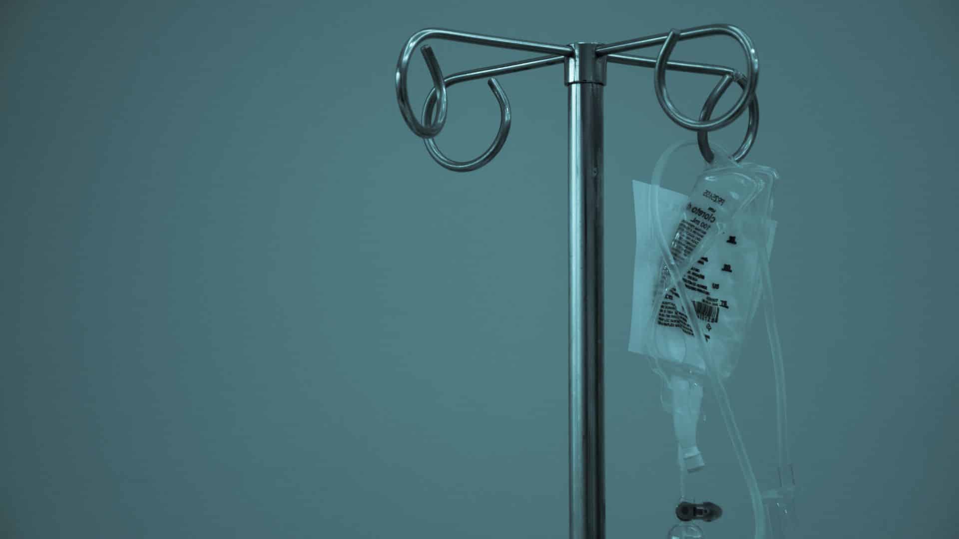 IV fluid bag hanging on a metal medical stand in a clinical setting
