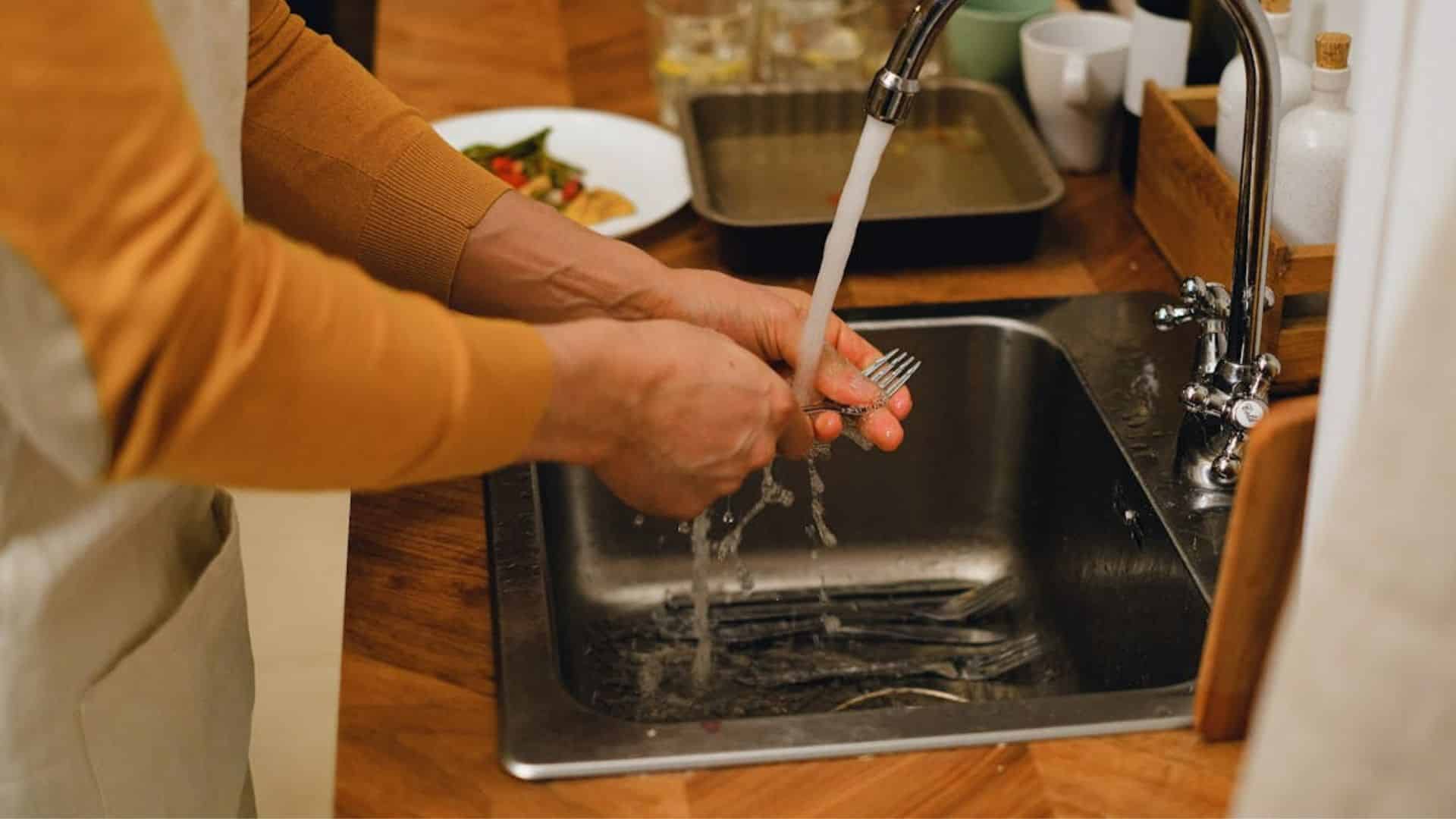 A person washing a fork in the sink