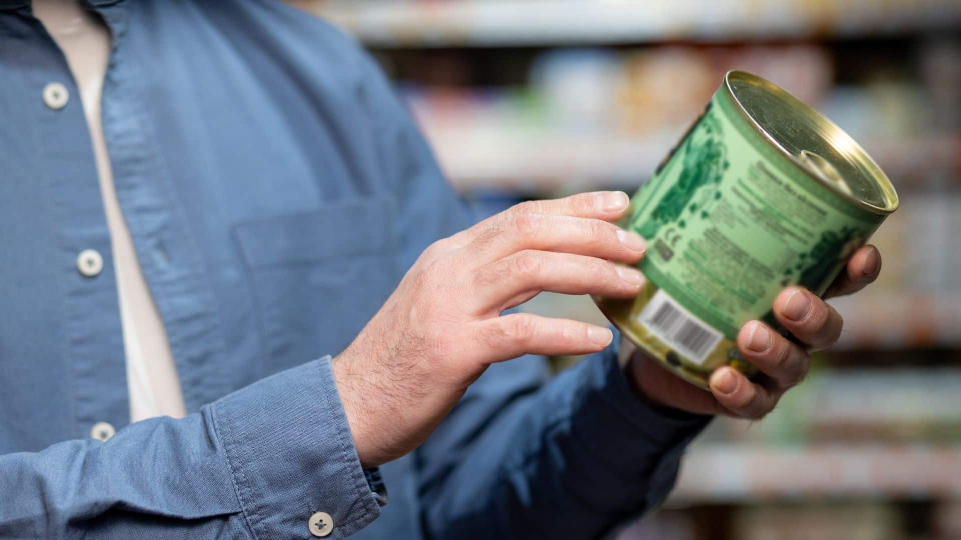Close-up of person examining canned food label in supermarket