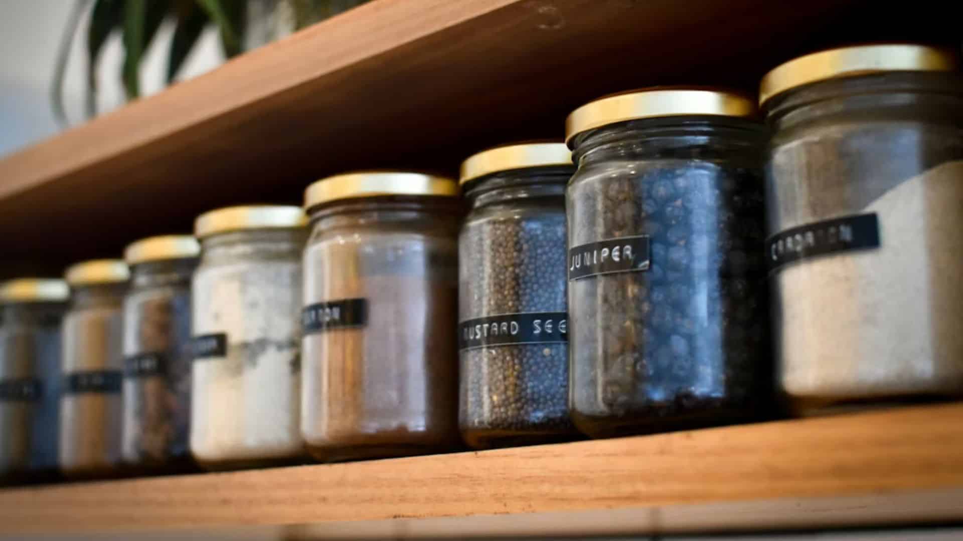 Assorted herbs and spices in glass jars on a wooden shelf
