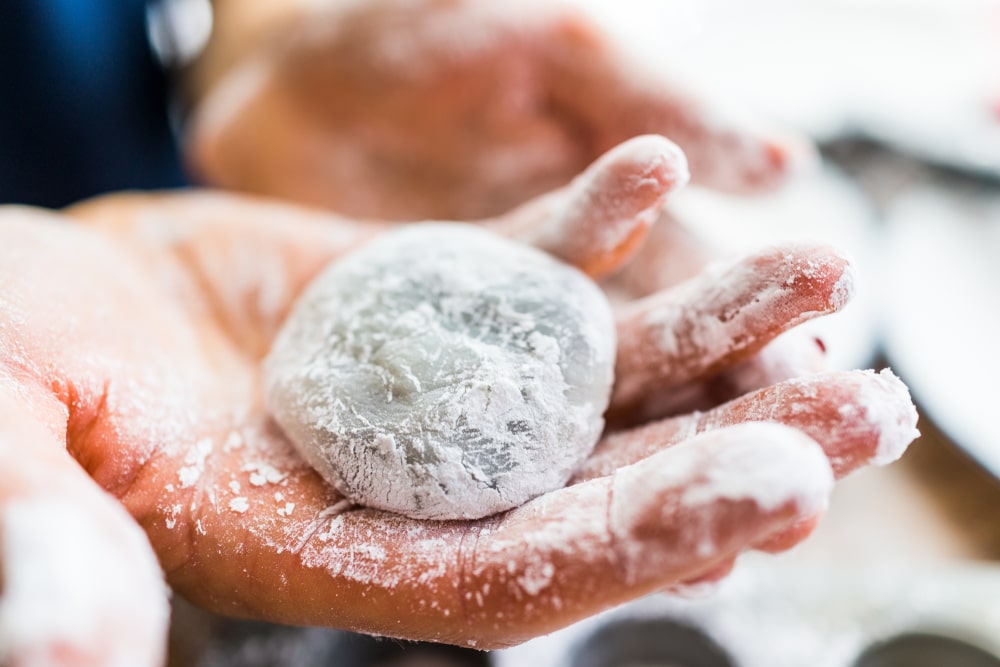 Hands shaping piece of mochi sticky glutinous rice cake dusted with starch flour to make dessert