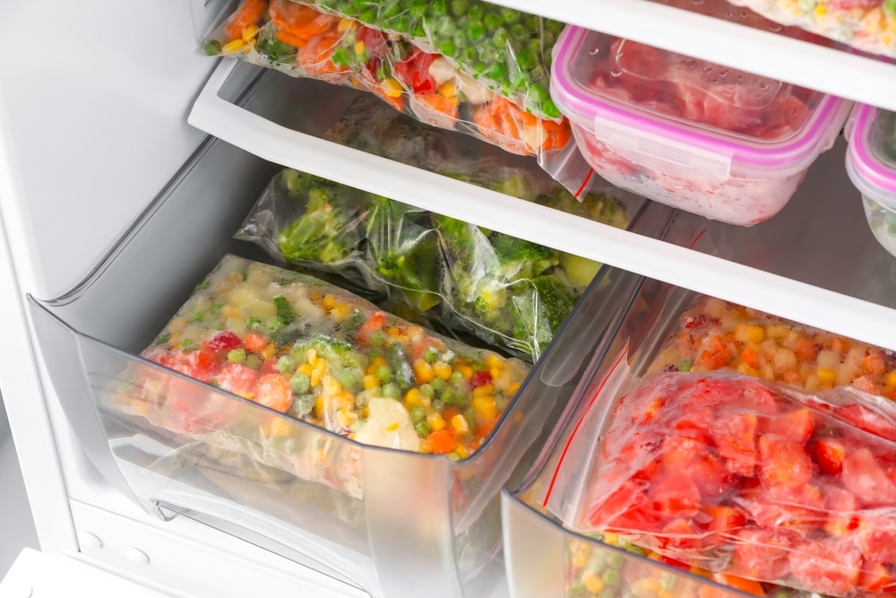 Plastic bags and containers with frozen vegetables in refrigerator