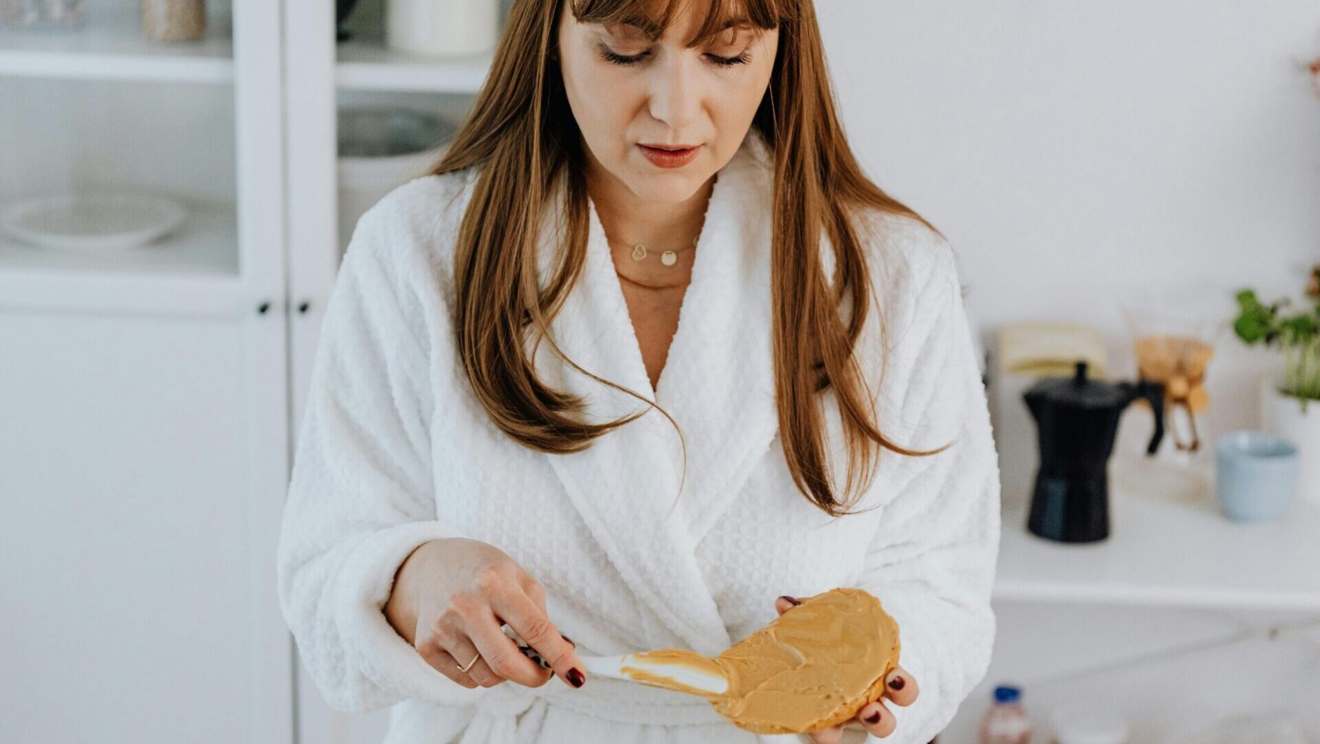 A person using a knife to spread peanut butter on a slice of toast on a table.