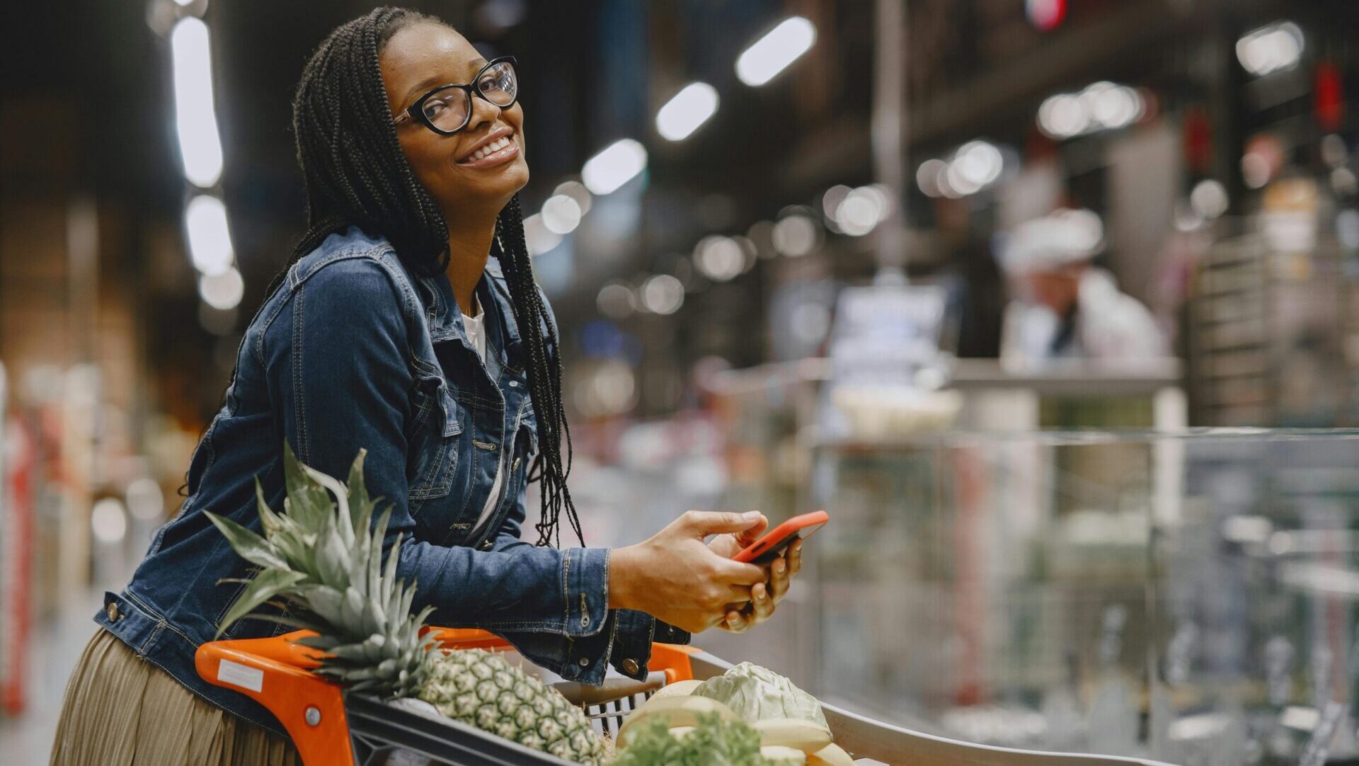 Smiling woman pushing a grocery cart and selecting items in a supermarket aisle.