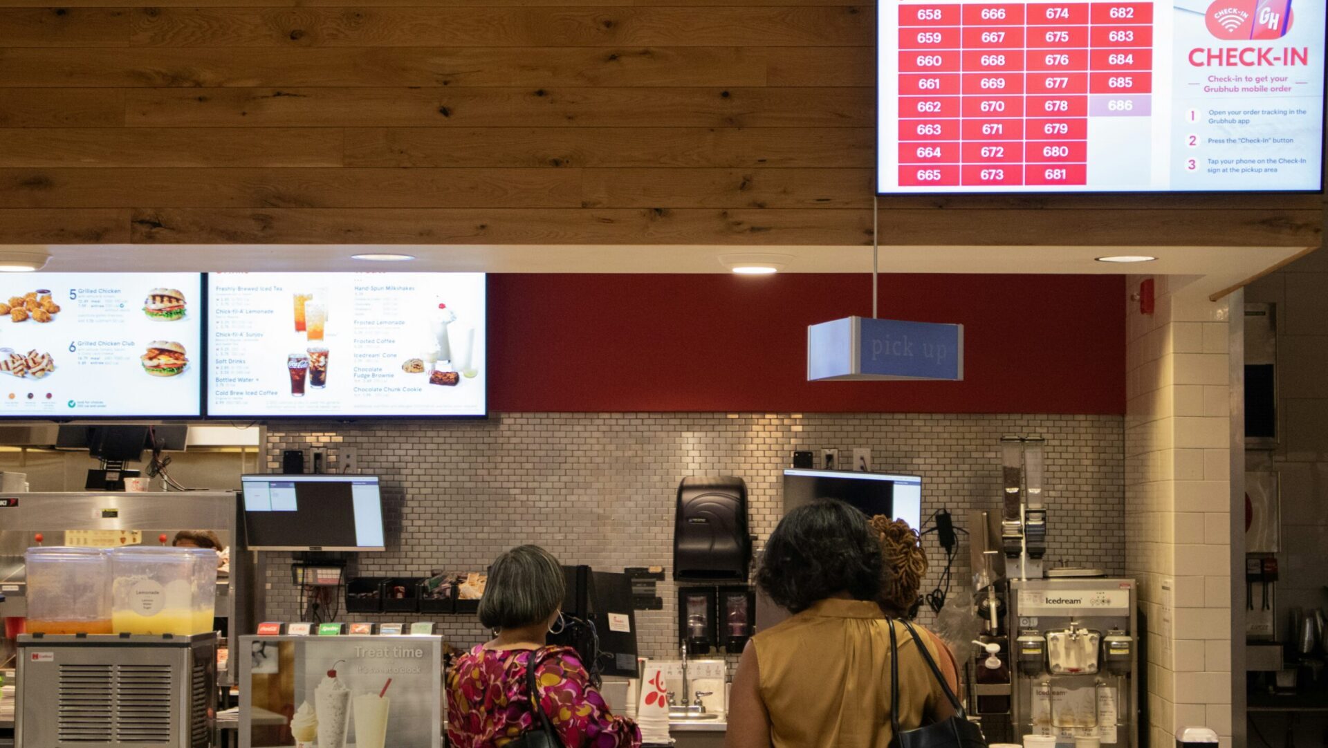 A couple of women standing in front of a fast food counter, looking at menu items and waiting to order.