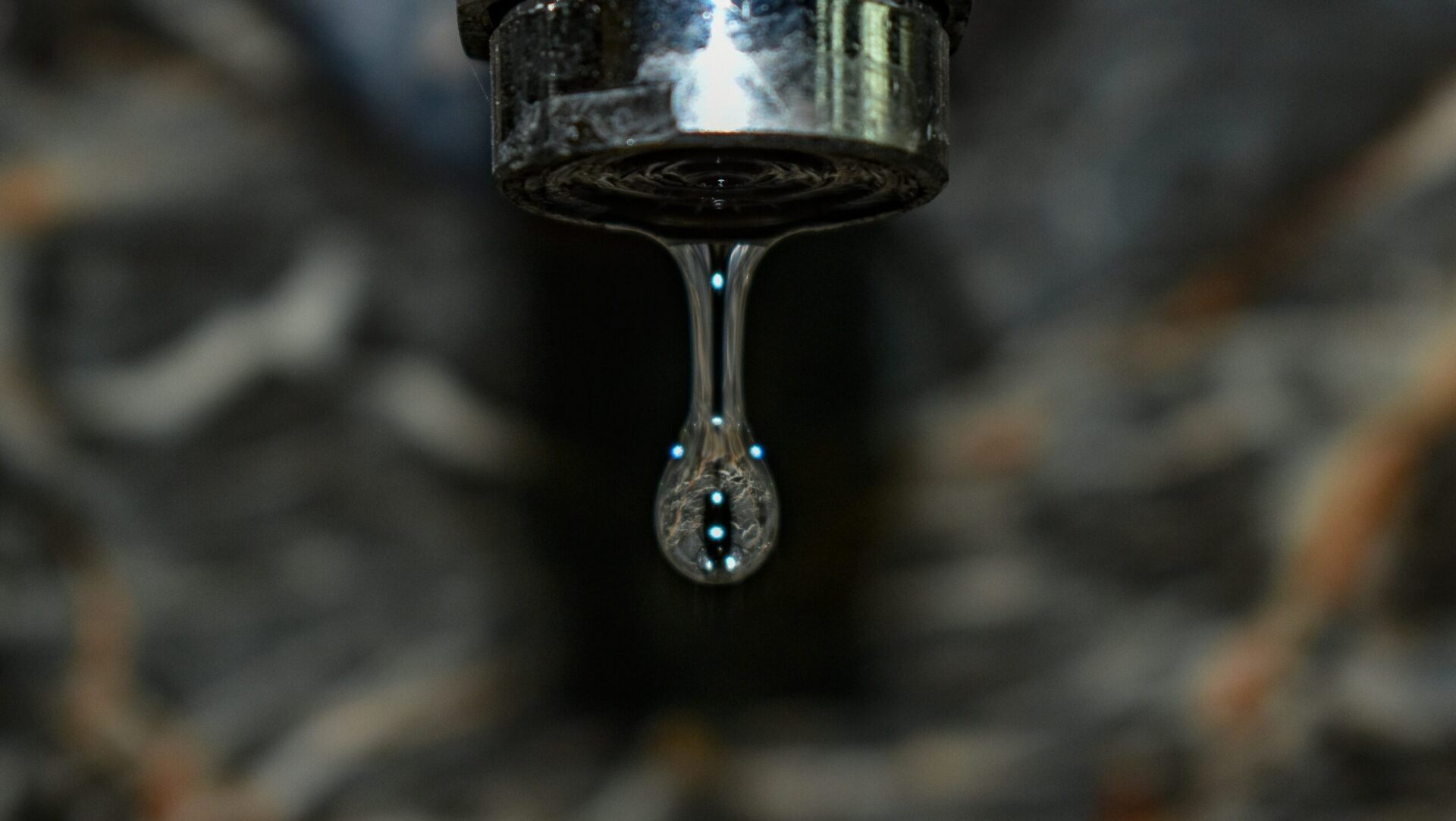 Water dripping steadily from a metal faucet, capturing motion and emphasizing water use or conservation.