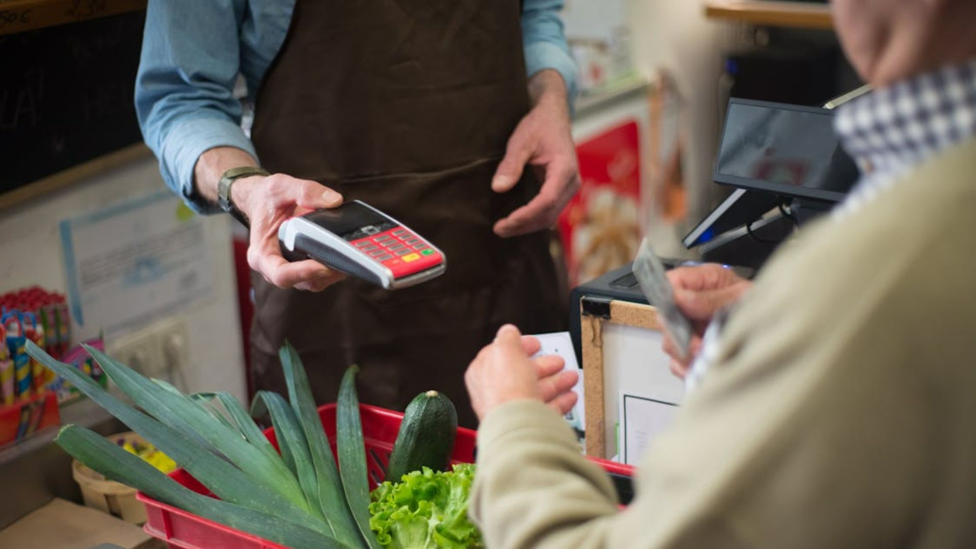 A cashier holds a card reader while a customer pays at a checkout counter