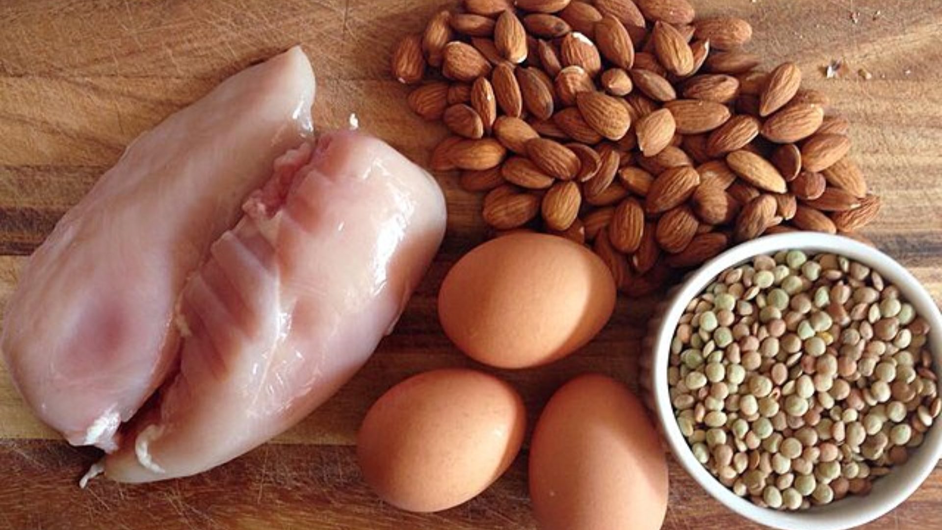 Chicken breasts, eggs, almonds, and lentils on a wooden surface.