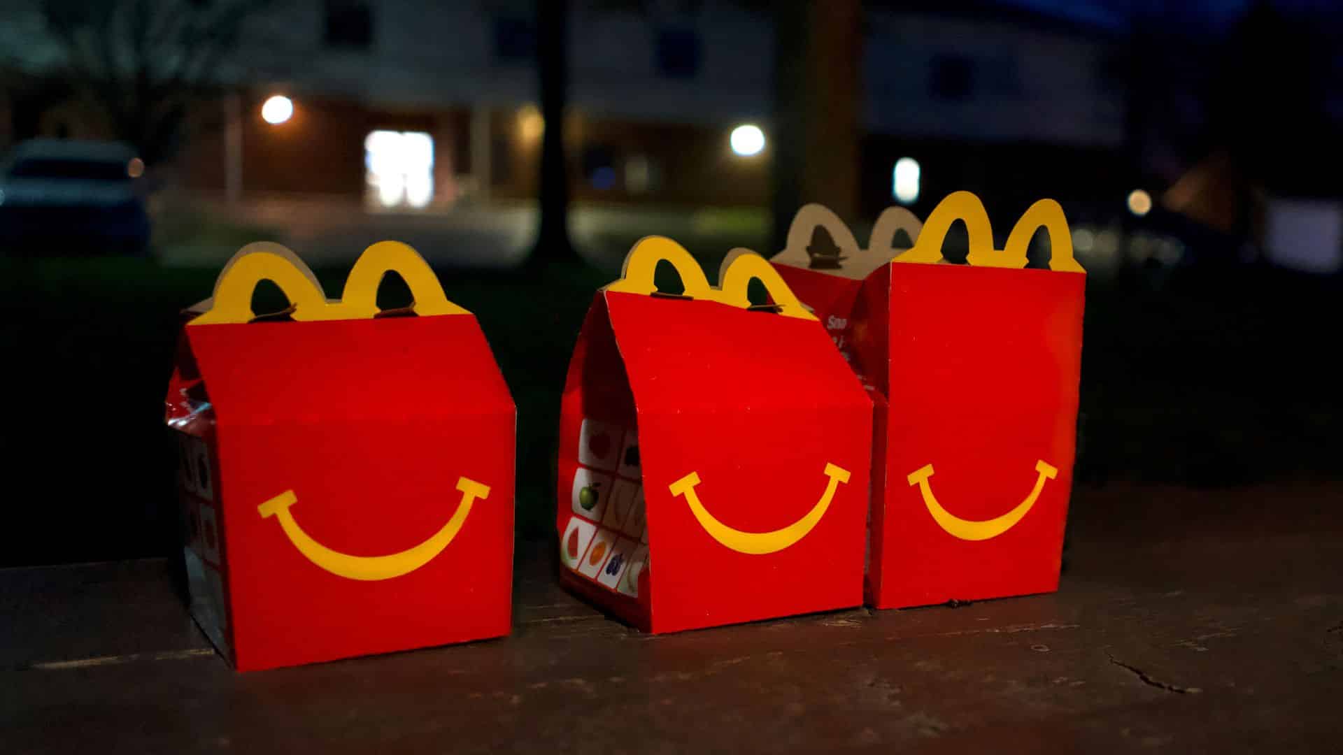 Image 2Three red McDonald’s Happy Meal boxes with yellow smile logos sit lined up on a ledge outdoors at night.