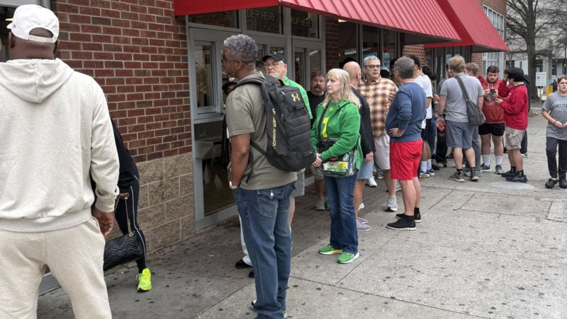 A long line of people waits outside a Waffle House under a red awning.