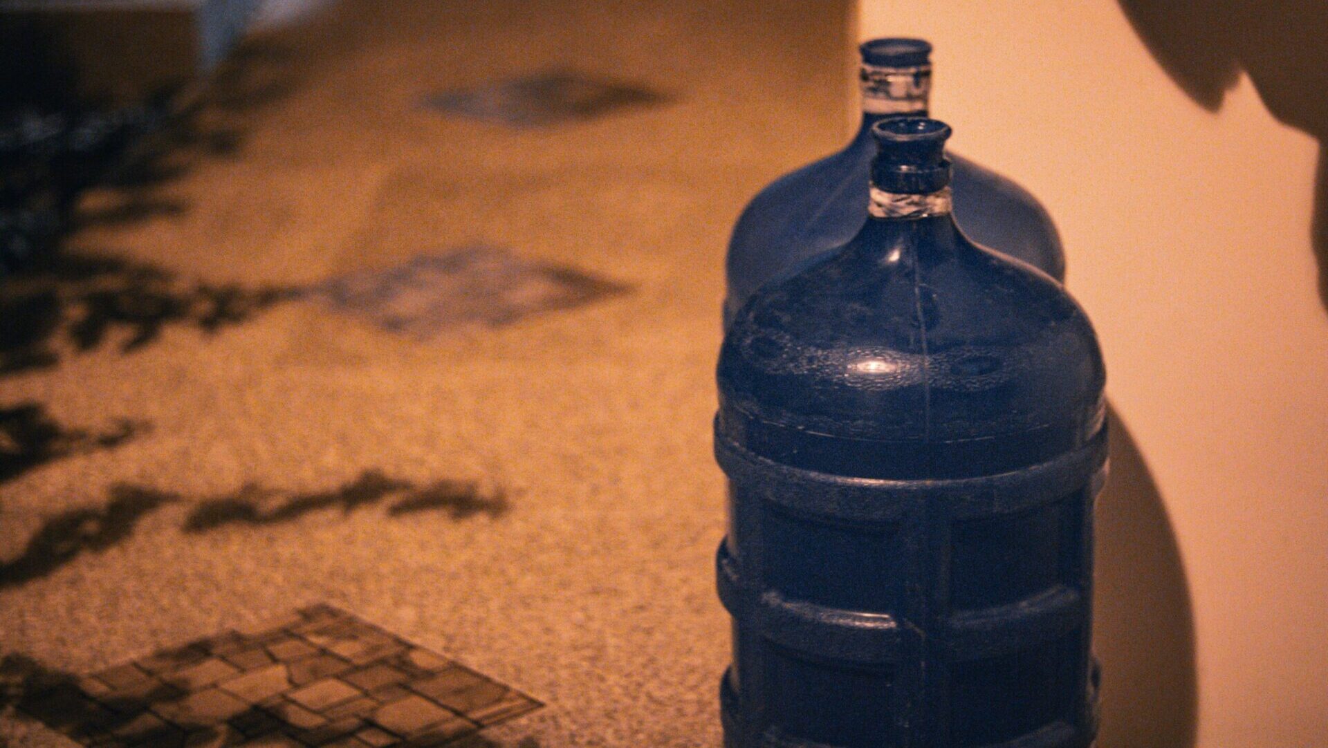 Blue plastic bottle resting on the floor beside a plain wall, creating a minimal and slightly industrial composition.