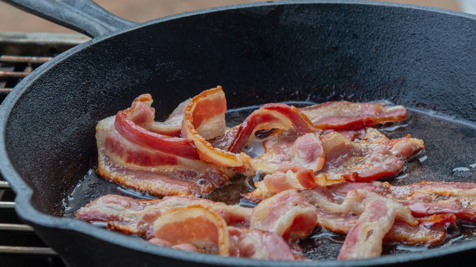 Strips of cooked bacon sizzling in a black pan.