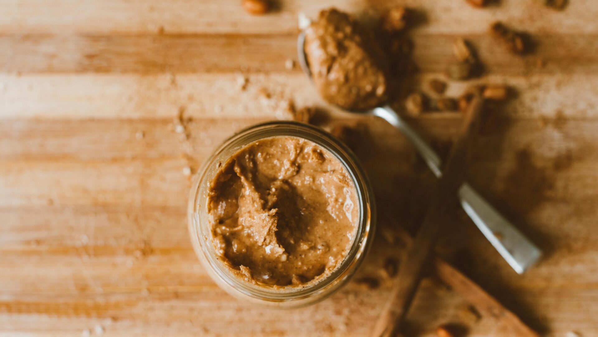 Clear glass jar filled with peanut butter placed on a surface with soft lighting.