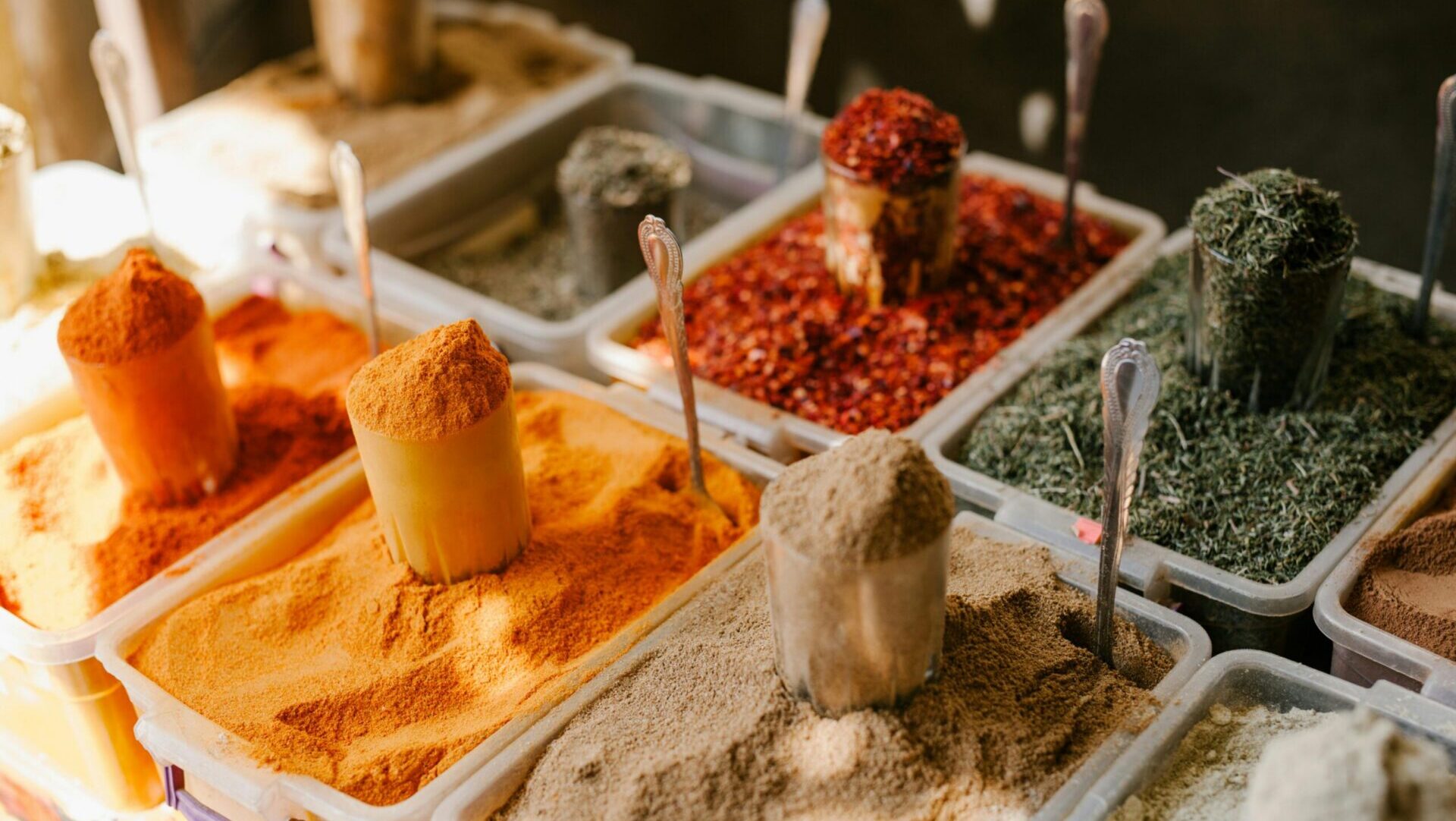 Assorted spices displayed at street market counter with bowls and scoops