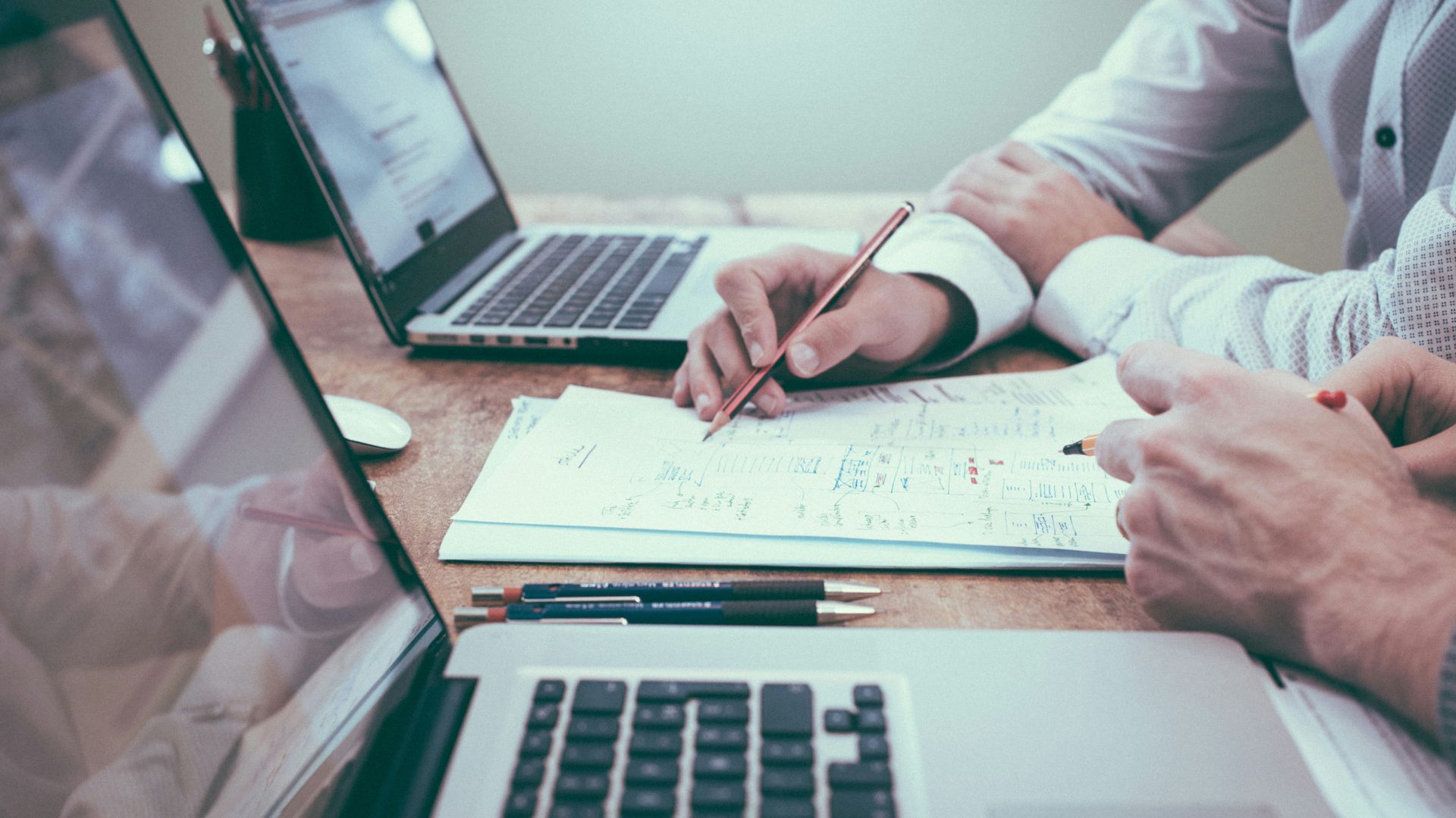 Person holding a pencil while working beside a laptop on a desk