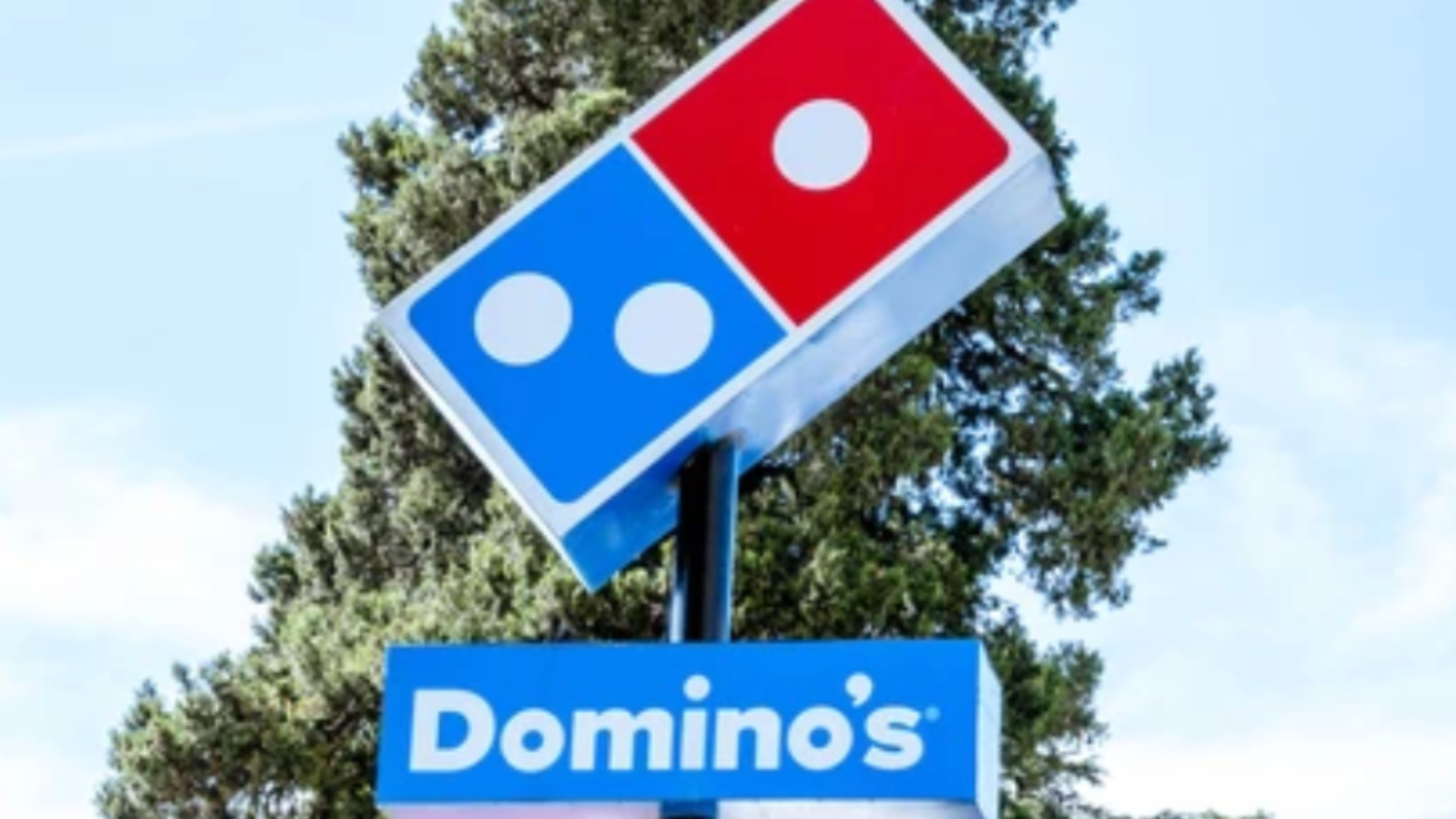 Domino’s Pizza signboard in front of trees and sky.