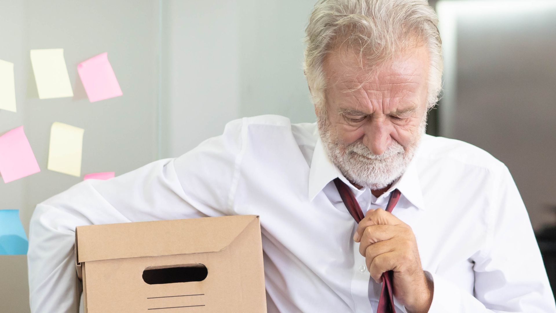 Senior employee carrying personal belongings in a box after job termination.