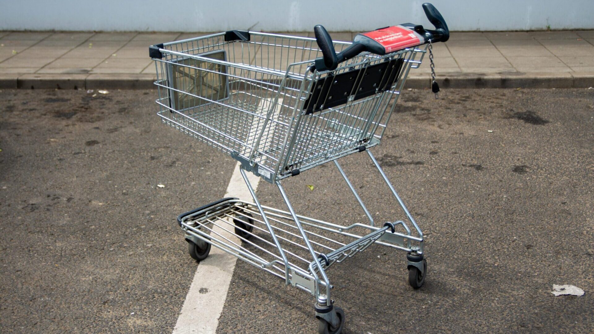 Empty shopping cart left in a parking lot with cars in the background.