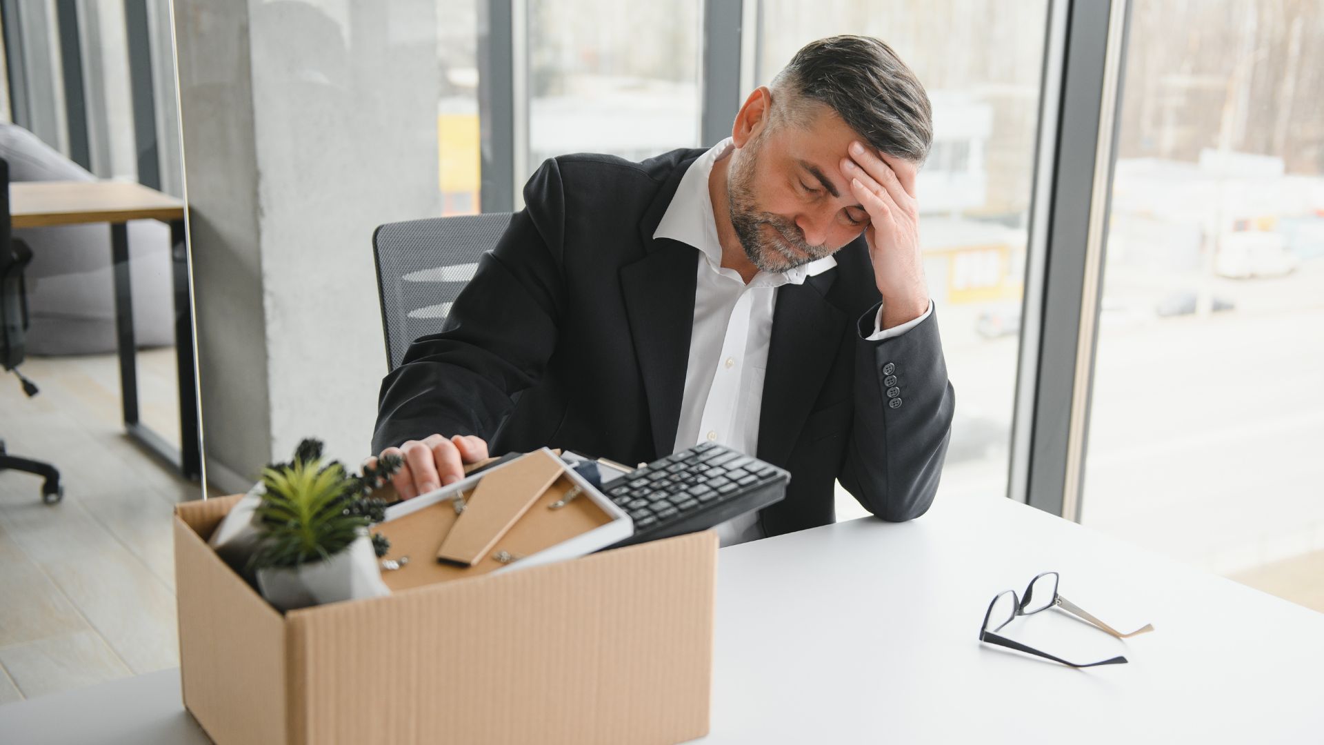 Older male employee sitting at desk reacting to termination notice