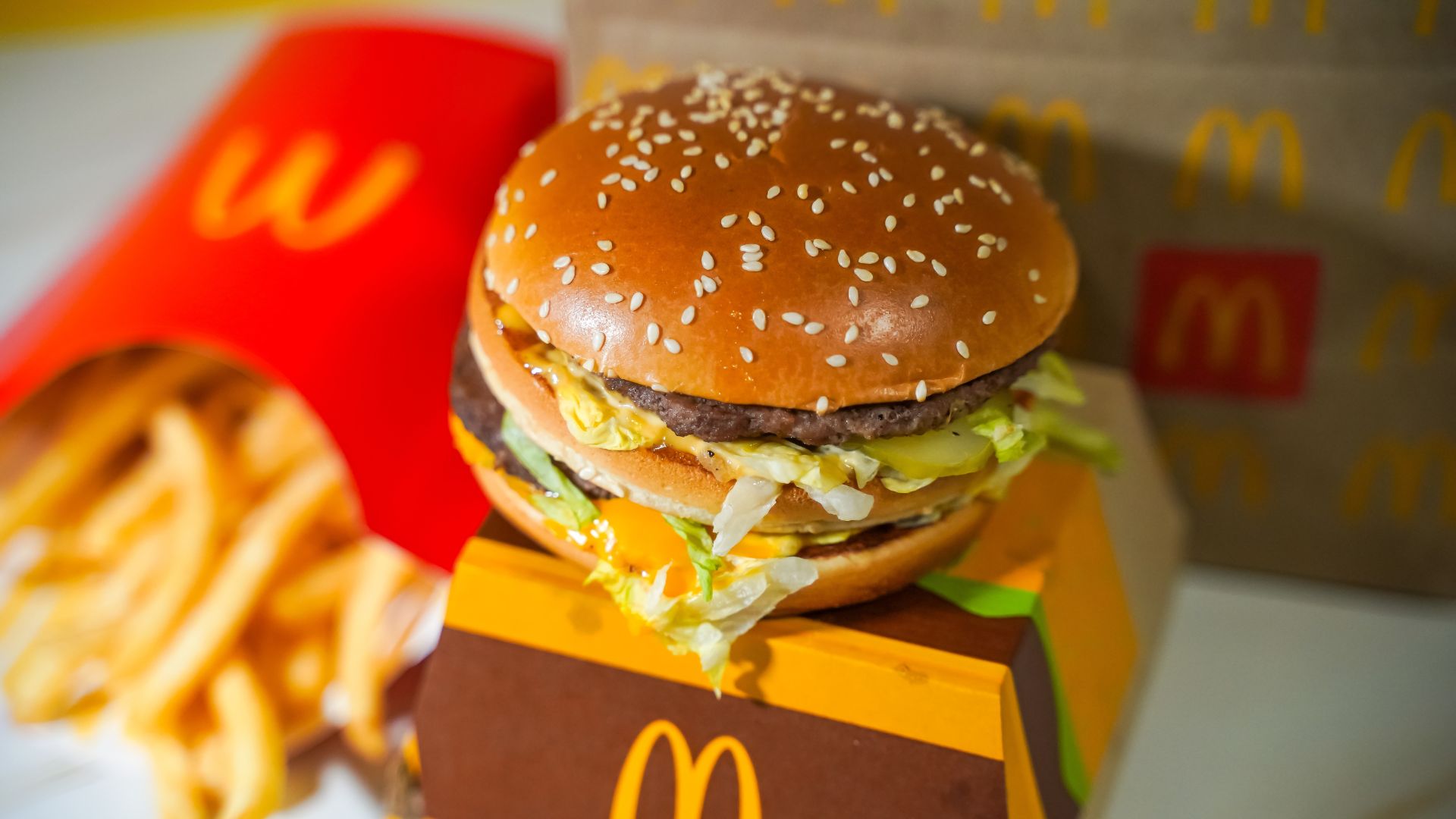 Close up of a McDonald’s burger with sesame seed bun, lettuce, cheese, and fries in background.