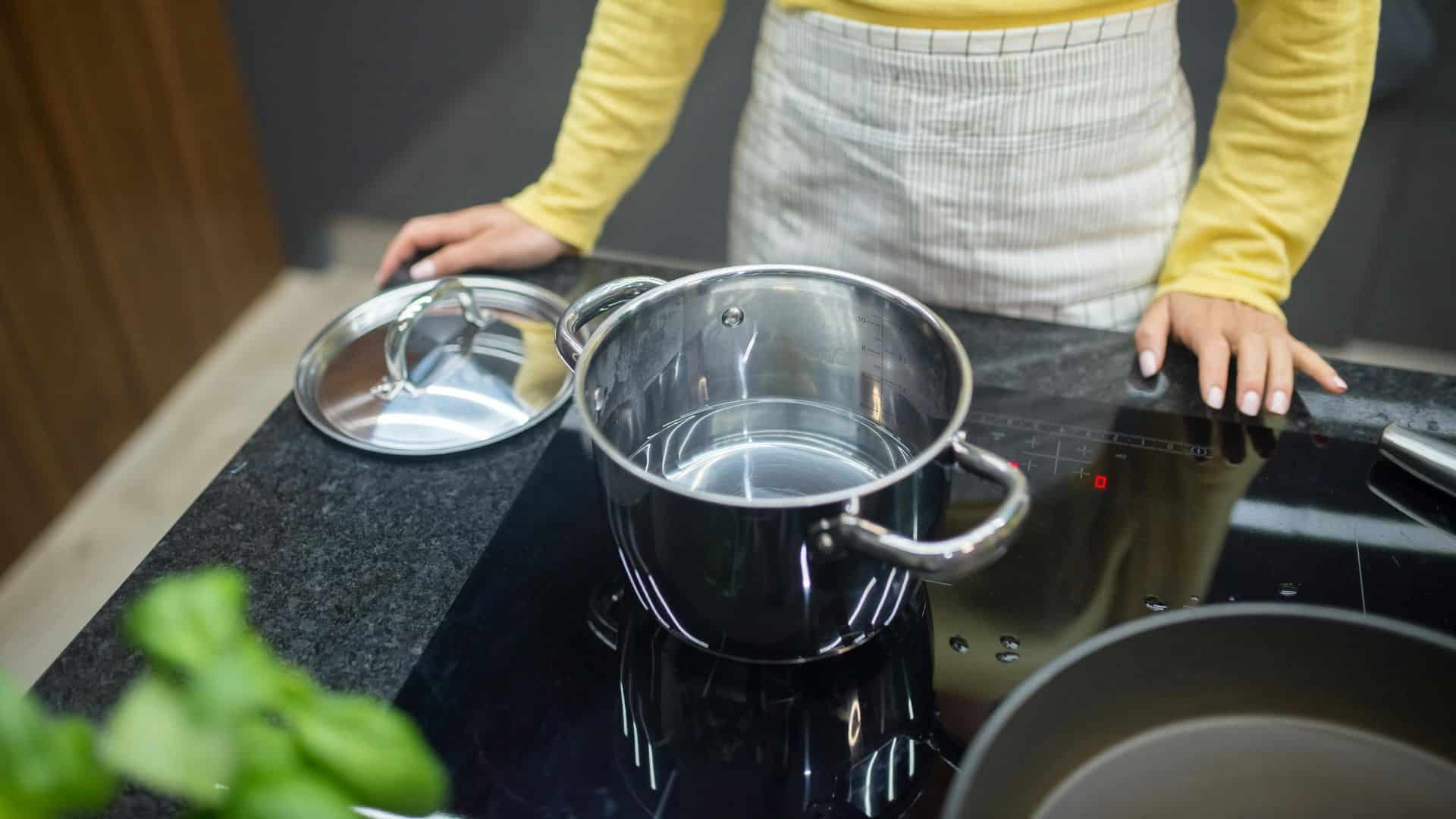 Woman using an induction cooktop with a steel pot in a kitchen